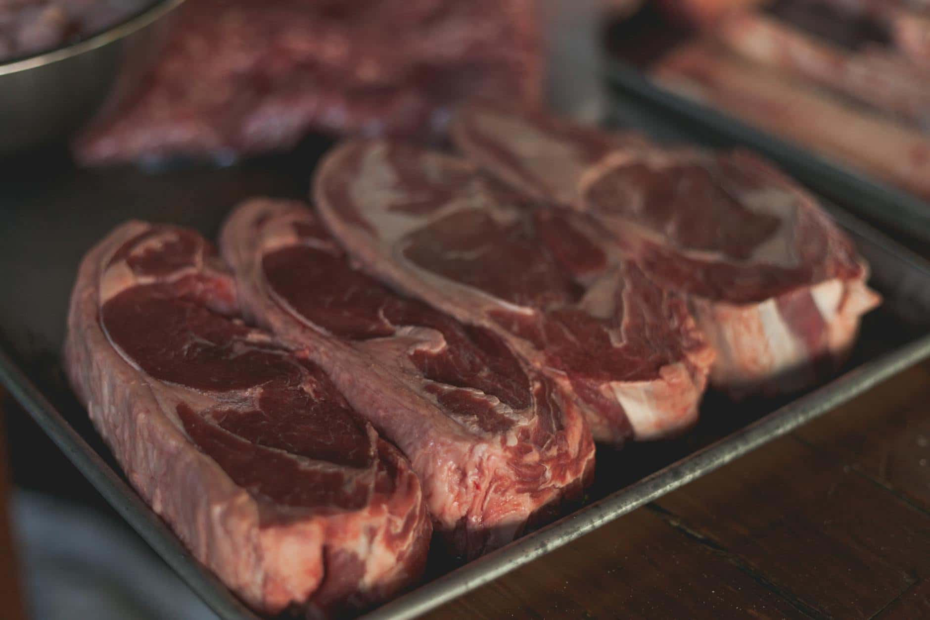 High-quality close-up image of raw steaks ready for cooking on a metal tray.