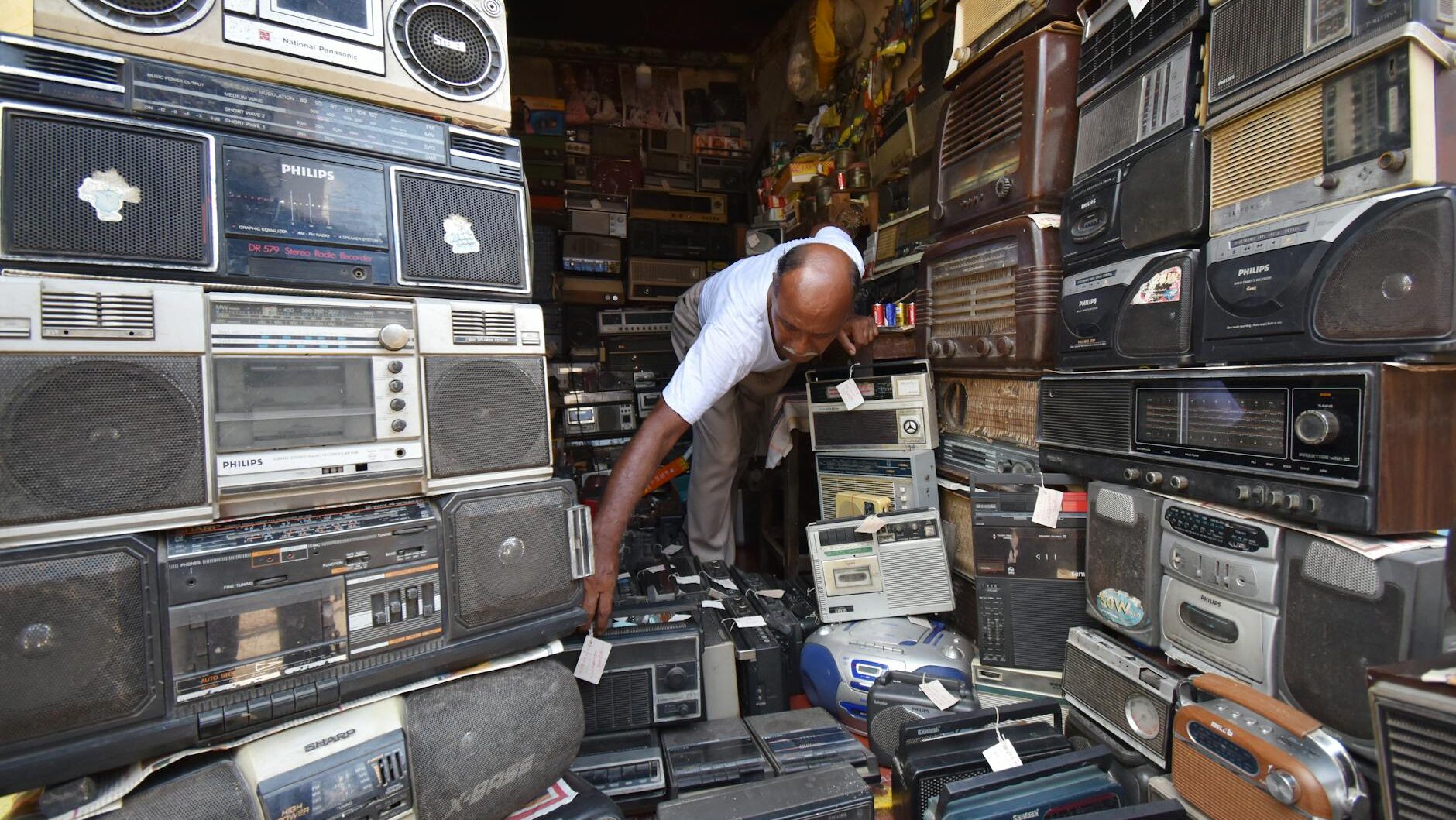 Man in Kolkata shop filled with vintage radios and electronics. Nostalgic atmosphere