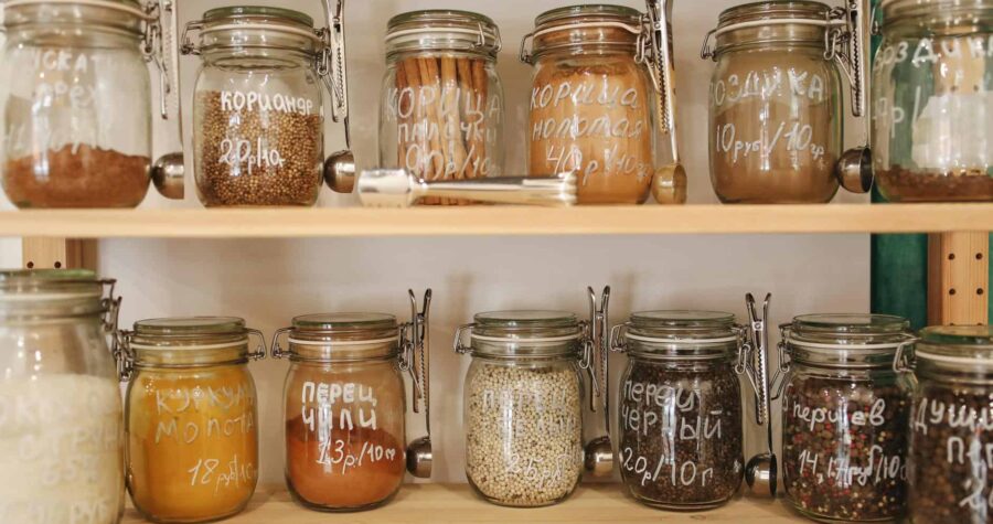 Organized pantry with glass jars holding a variety of spices and ingredients on wooden shelves.