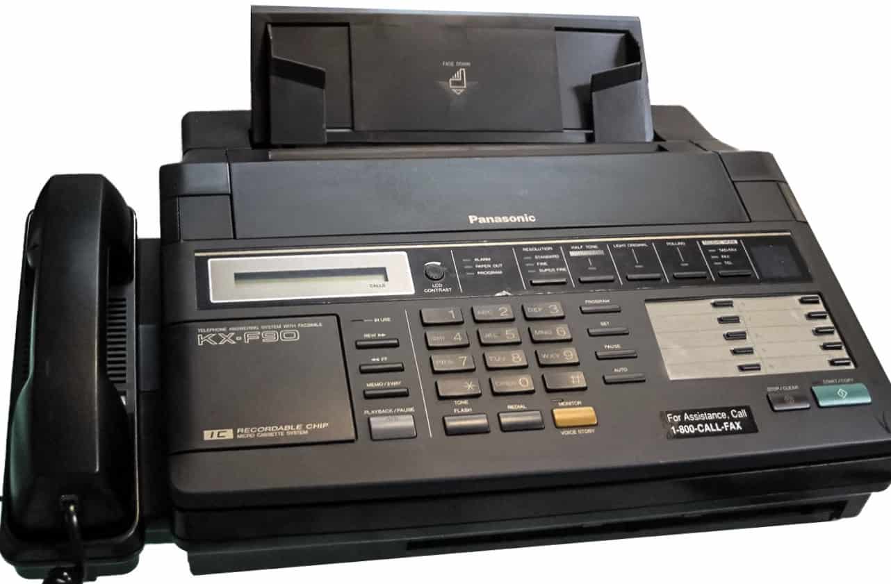 A Panasonic fax machine, with a phone attached, buttons for dialing, sending, and receiving faxes, a screen displaying information, a compartment for paper or a cassette, various settings for fax quality, and a logo reading "KX-F90," placed on a surface with a white background