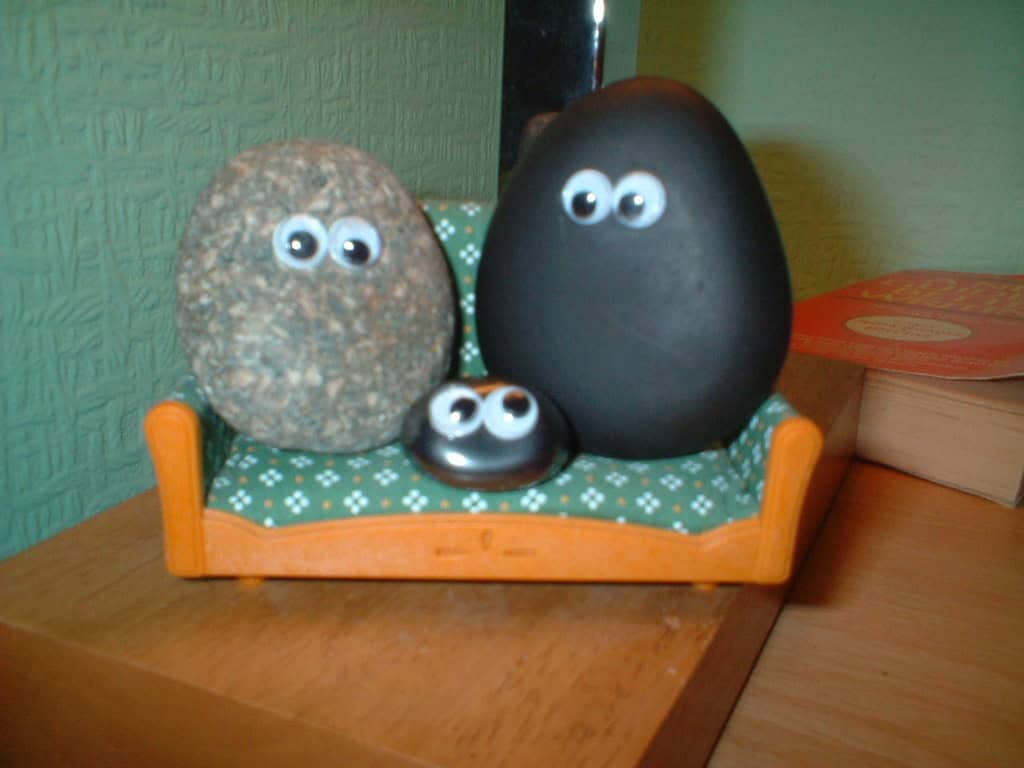 Three rocks with googly eyes sitting on a small couch, creating a playful and quirky scene, two larger rocks sitting on either side of a smaller rock, all arranged as if they were a family, the rocks are arranged as characters with eyes, showcasing a fun and creative display