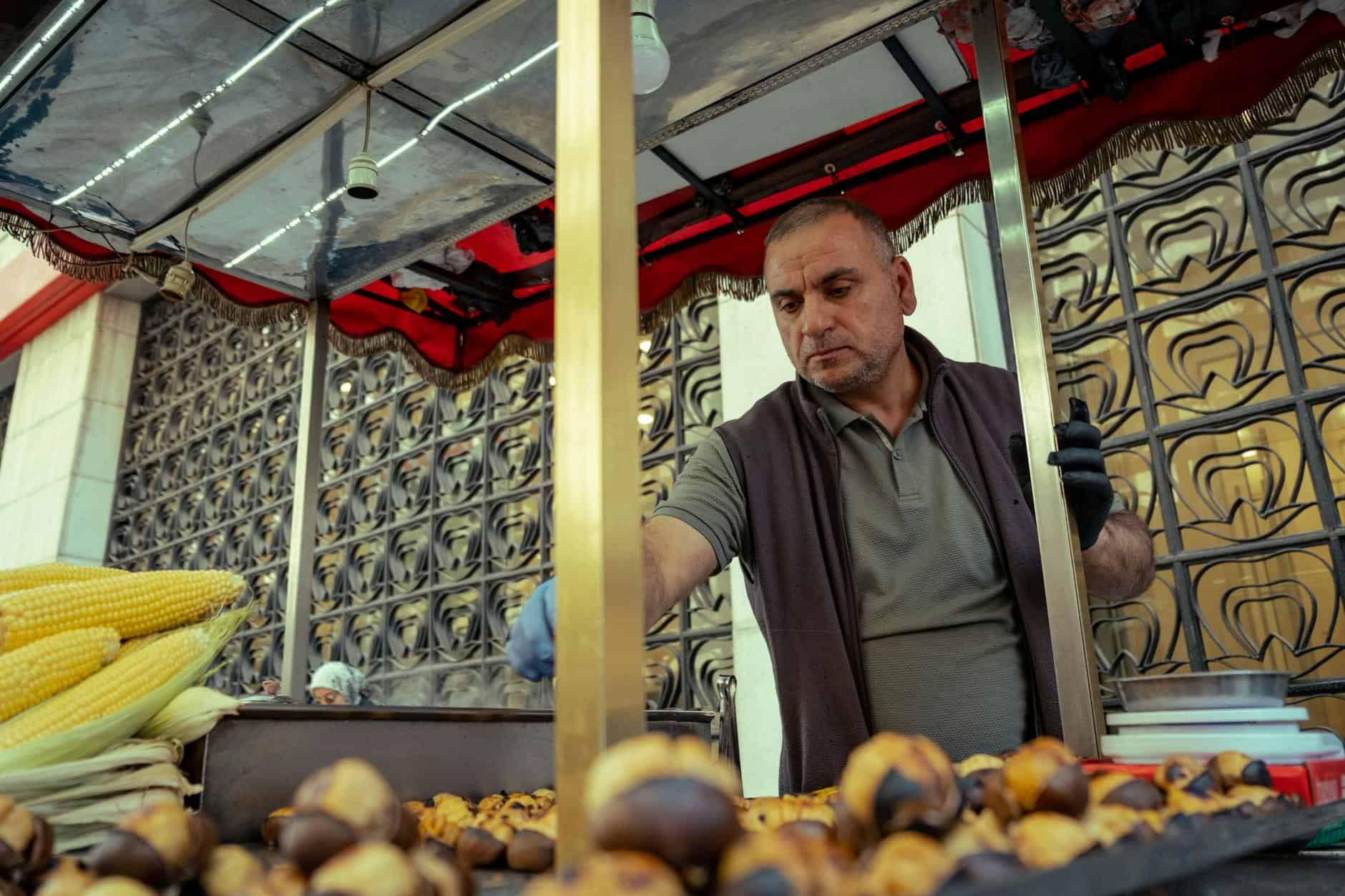Street vendor roasting chestnuts and corn in an urban setting, offering a warm food experience.