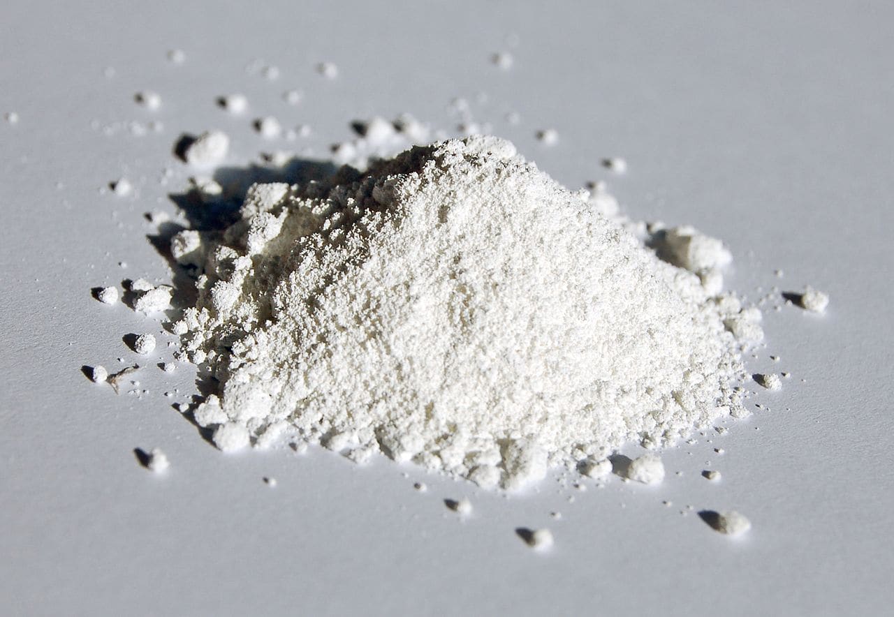 A pile of white powder, finely ground and spread on a flat surface, the powder appears soft and smooth, scattered slightly around the pile, emphasizing the fine texture of the material