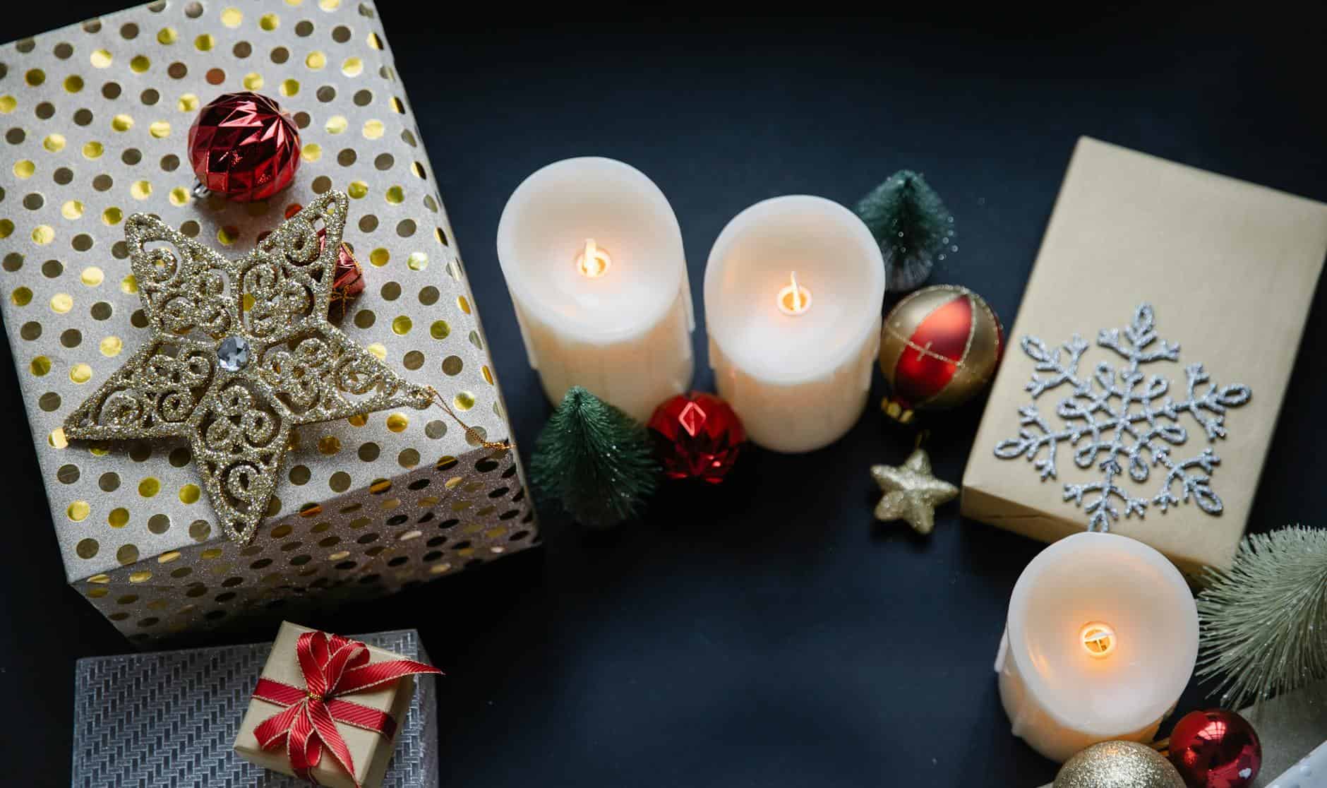 Top view of festive Christmas gifts, candles, and decorations on a black background.