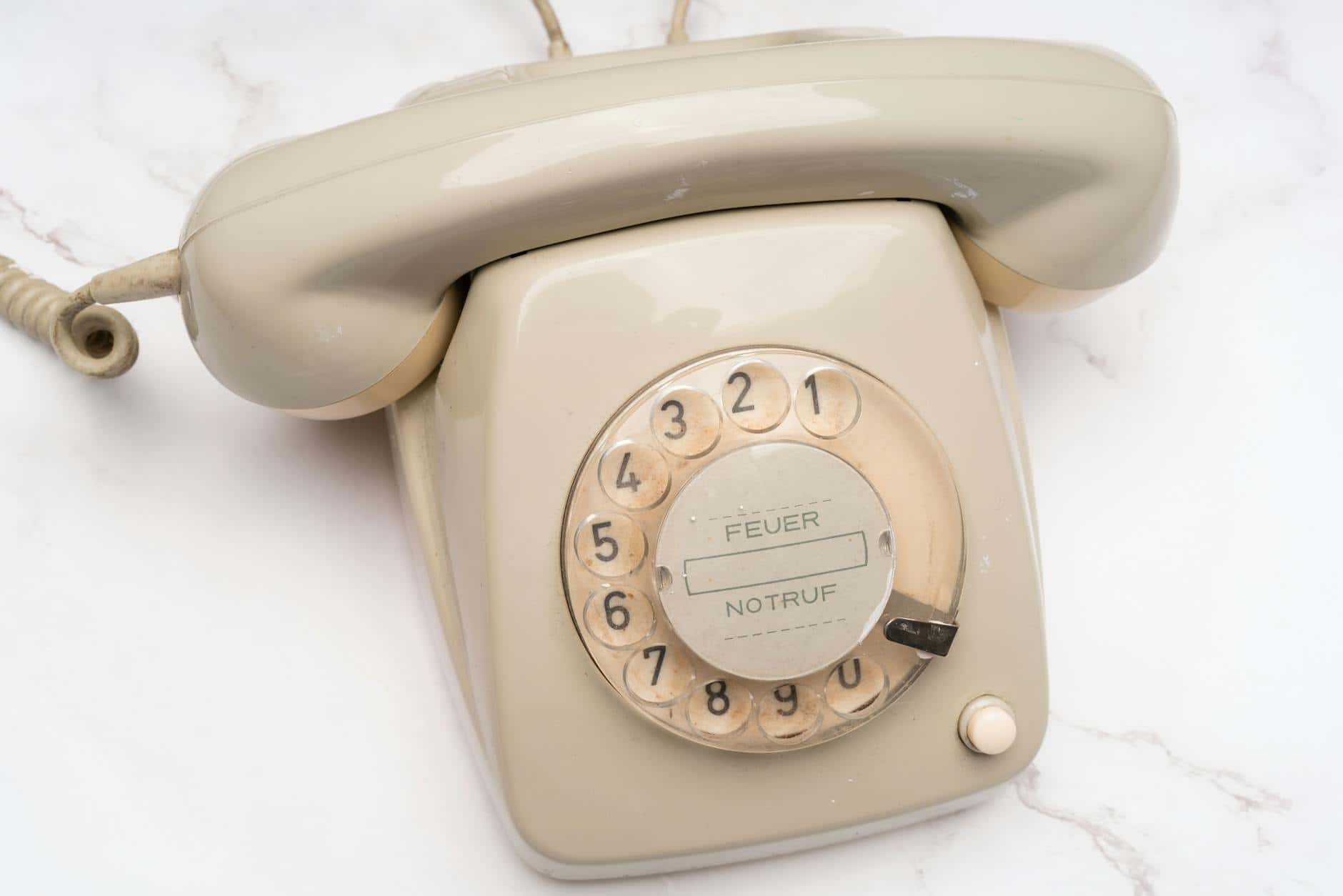 Vintage beige rotary dial telephone placed on a white marble surface exemplifying classic communication tech.