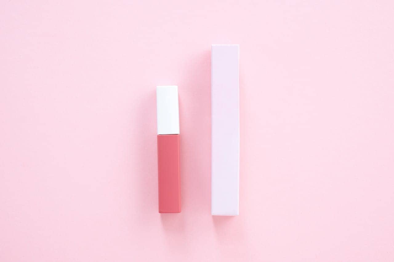 Pink lip gloss tube with white cap, placed beside matching pink box, set on a light pink background, minimal and modern design, beauty product display