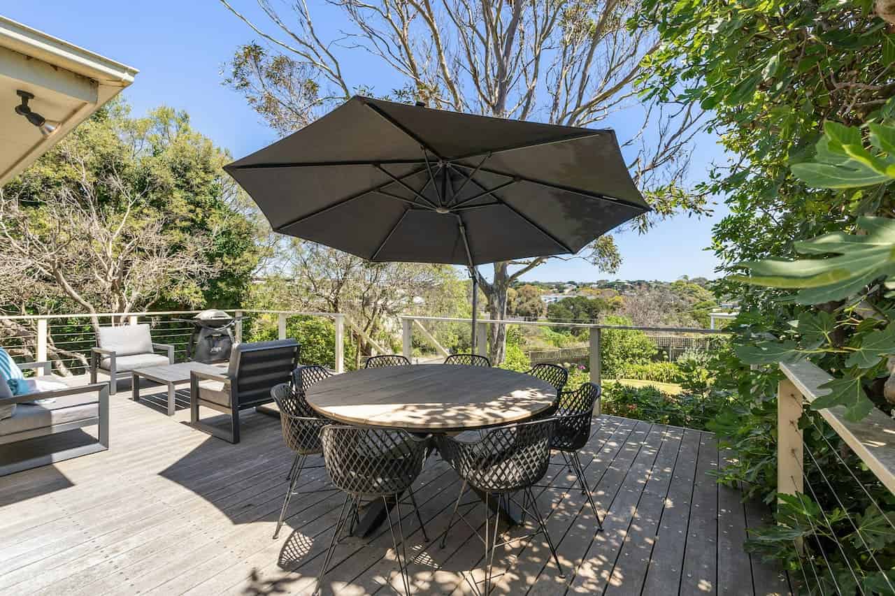 Wooden deck with round dining table, pop-up canopy for shade, modern wire chairs, lounge furniture, and panoramic views of trees and hillside