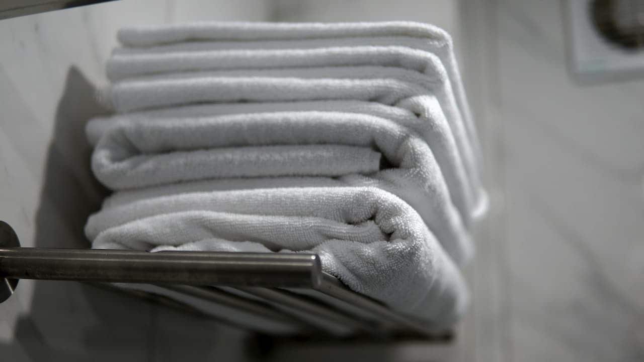 Stack of folded white towels on a metal rack in a bathroom, neatly arranged on a white shelf
