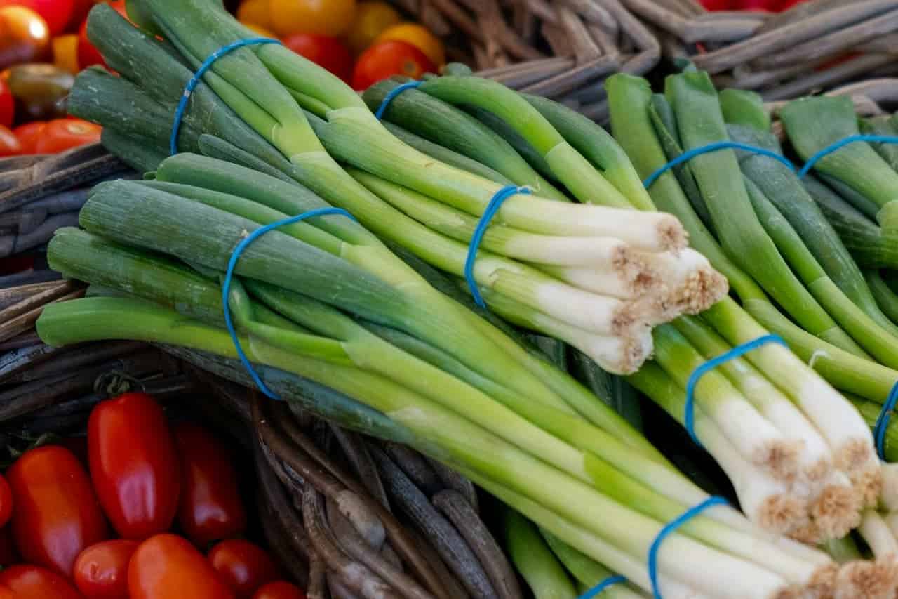 Bunches of fresh green chives tied with blue rubber bands displayed in wicker baskets alongside red cherry tomatoes at market