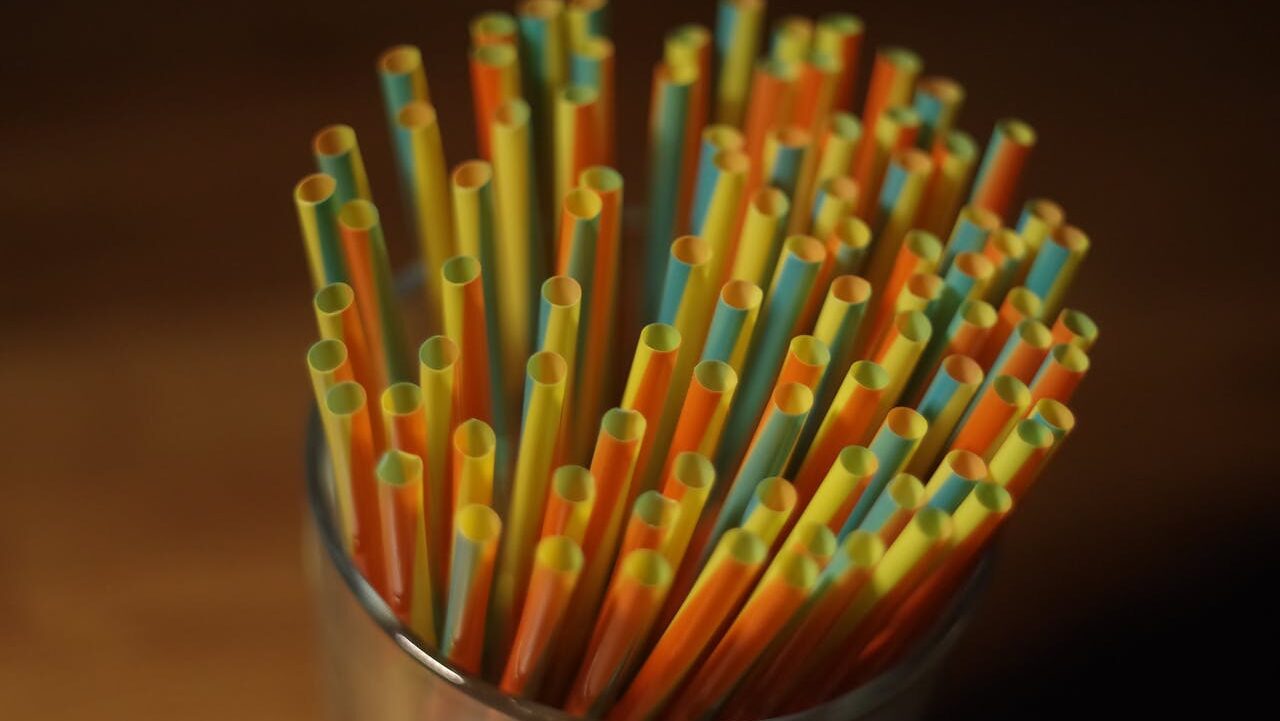 Colorful plastic straws arranged in a glass container, with various shades of yellow, orange, and blue straws standing upright, close-up shot, the straws are stacked closely together