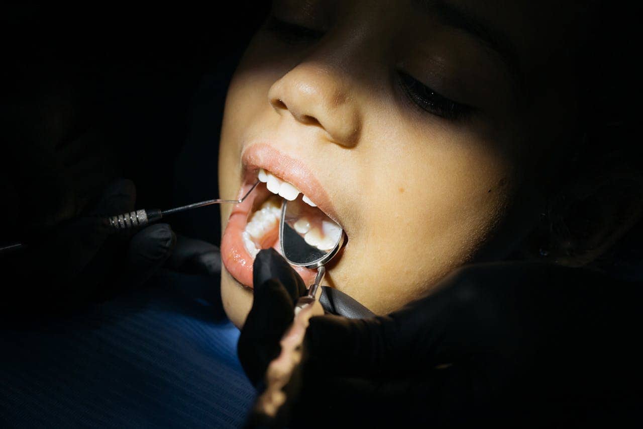 A close-up of a person receiving a dental checkup, the dentist using dental tools, including a mirror and scaler, to inspect the patient's teeth, the patient's mouth is open, showing healthy teeth, the scene highlights dental care and hygiene in a clinical setting