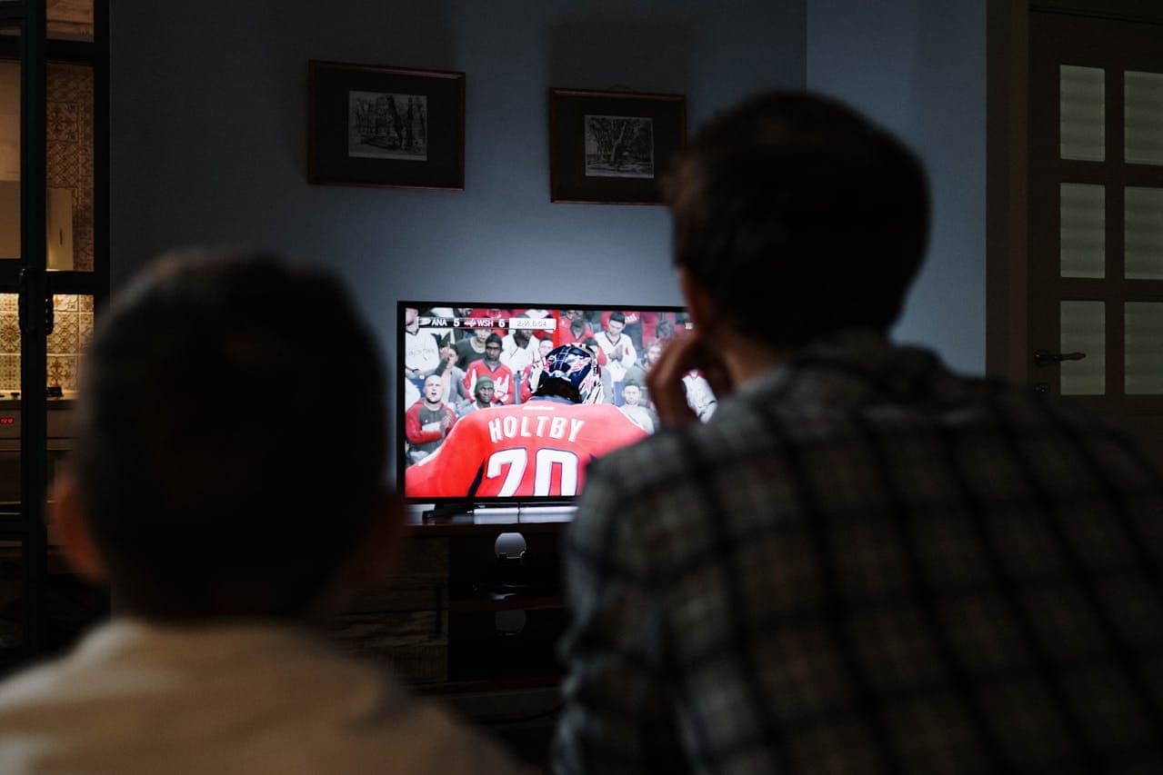 Two people watching hockey game on television showing player with jersey number 70 and name Holtby in darkened room