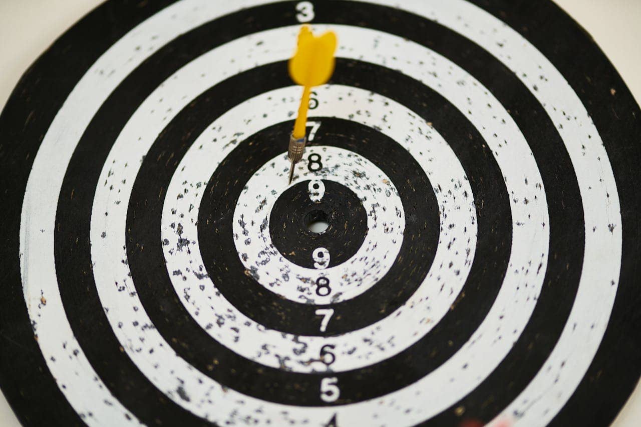 Yellow dart stuck in the number 9 section of a black and white dartboard, concentric circles of the dartboard visible, the dart's position clearly showing in the target zone