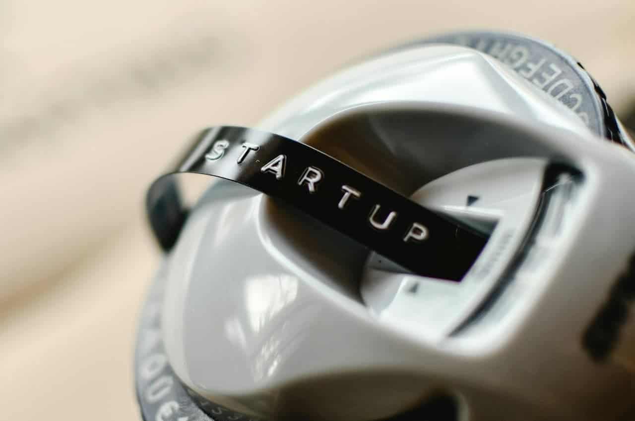 The image shows a close-up of a white object with a black "STARTUP" label, the object has a round, shiny surface, the label is clear and embossed, with the focus on the lettering, the background is blurred, giving the impression of a sleek and modern product design
