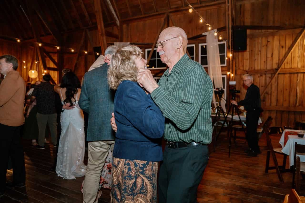 An elderly couple dancing together at a wedding reception, warm, intimate atmosphere, dimly lit barn with string lights