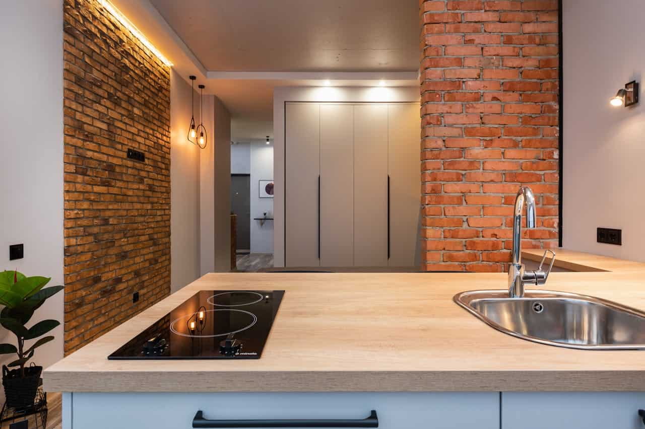 Modern kitchen with exposed brick walls, wooden countertop, induction cooktop, stainless sink, and minimalist cabinetry in industrial-style apartment