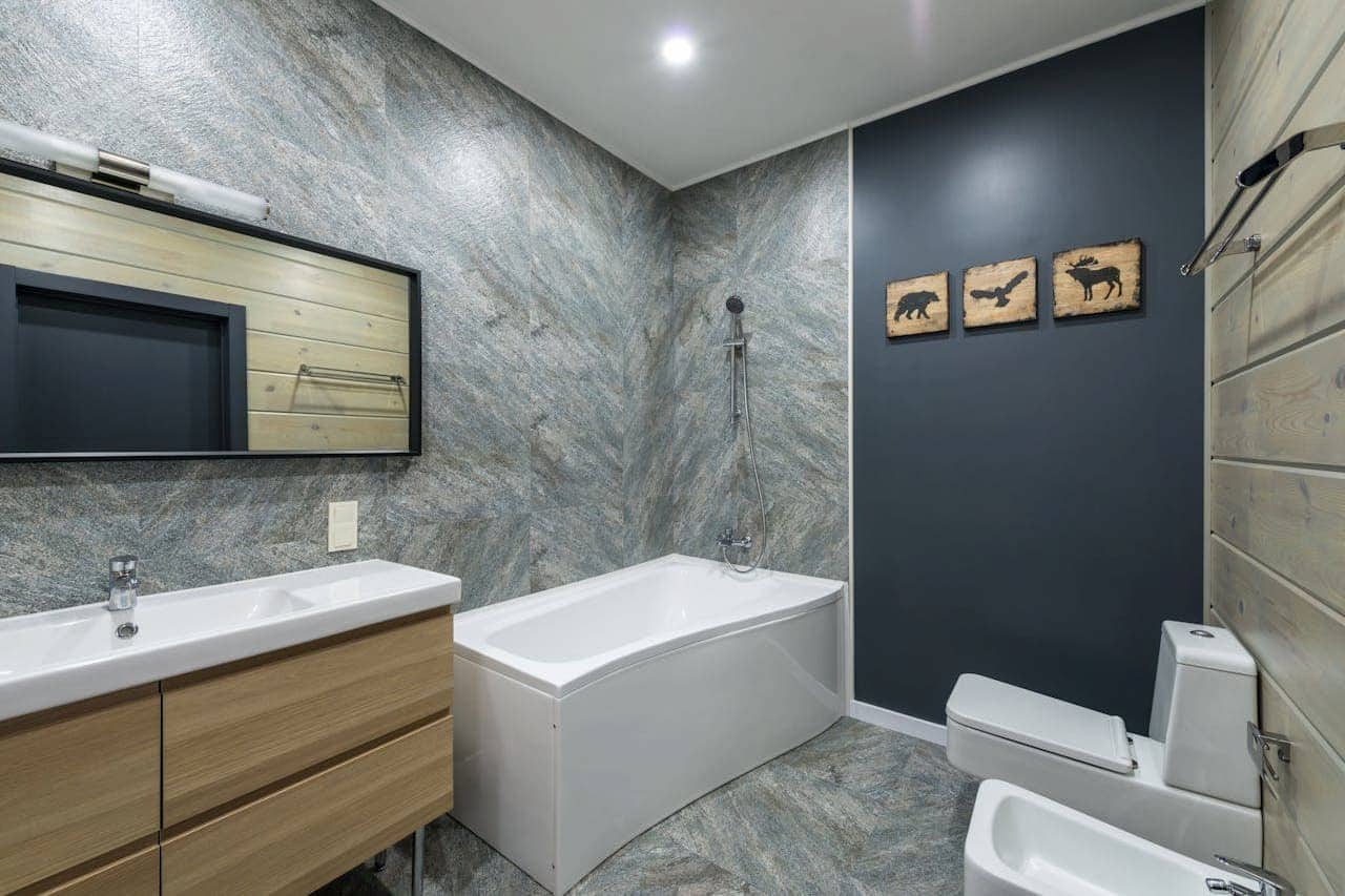 Modern bathroom with marble-effect walls, white bathtub, wooden vanity, navy accent wall featuring wildlife silhouette artwork