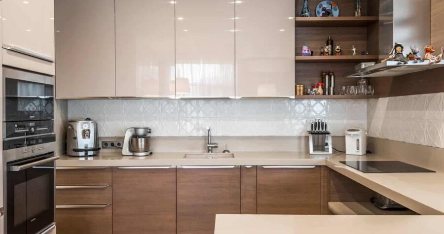 Modern L-shaped kitchen with glossy white upper cabinets, wooden lower cabinets, beige countertops, built-in appliances, and decorative shelving