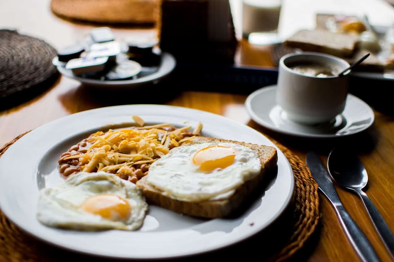 Breakfast plate with fried eggs on toast, beans with cheese, beside coffee cup on wooden table