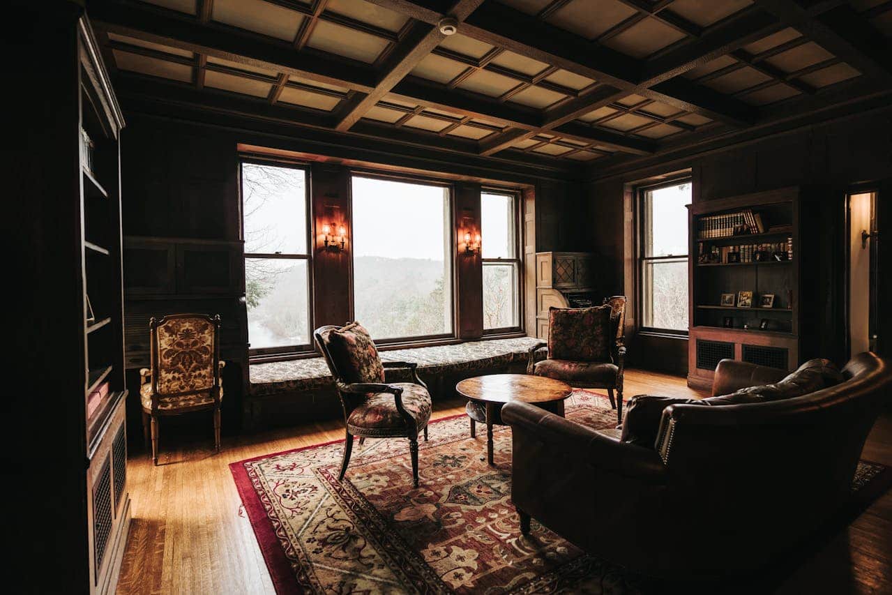 Cozy vintage living room with a wooden ceiling, two comfortable armchairs and a leather couch, a small round coffee table, a large rug, bookshelves on the side