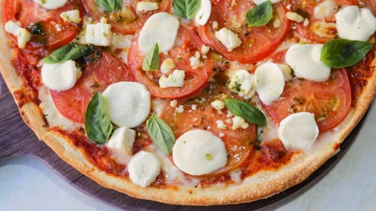 Cashew cheese pizza topped with fresh tomato slices, white cheese dollops, and green basil leaves on wooden surface
