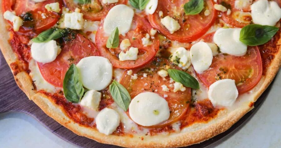 Cashew cheese pizza topped with fresh tomato slices, white cheese dollops, and green basil leaves on wooden surface