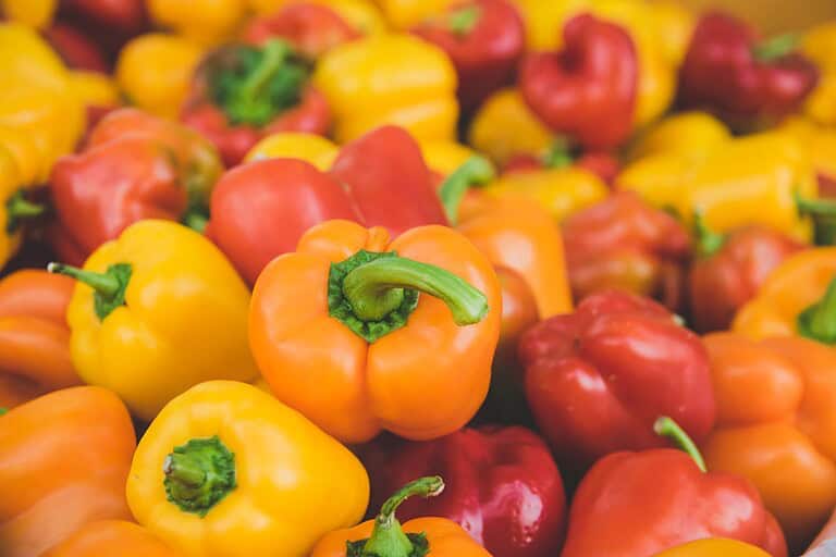 Colorful bell peppers in yellow, orange, and red varieties clustered together, showing their glossy surfaces and green stems