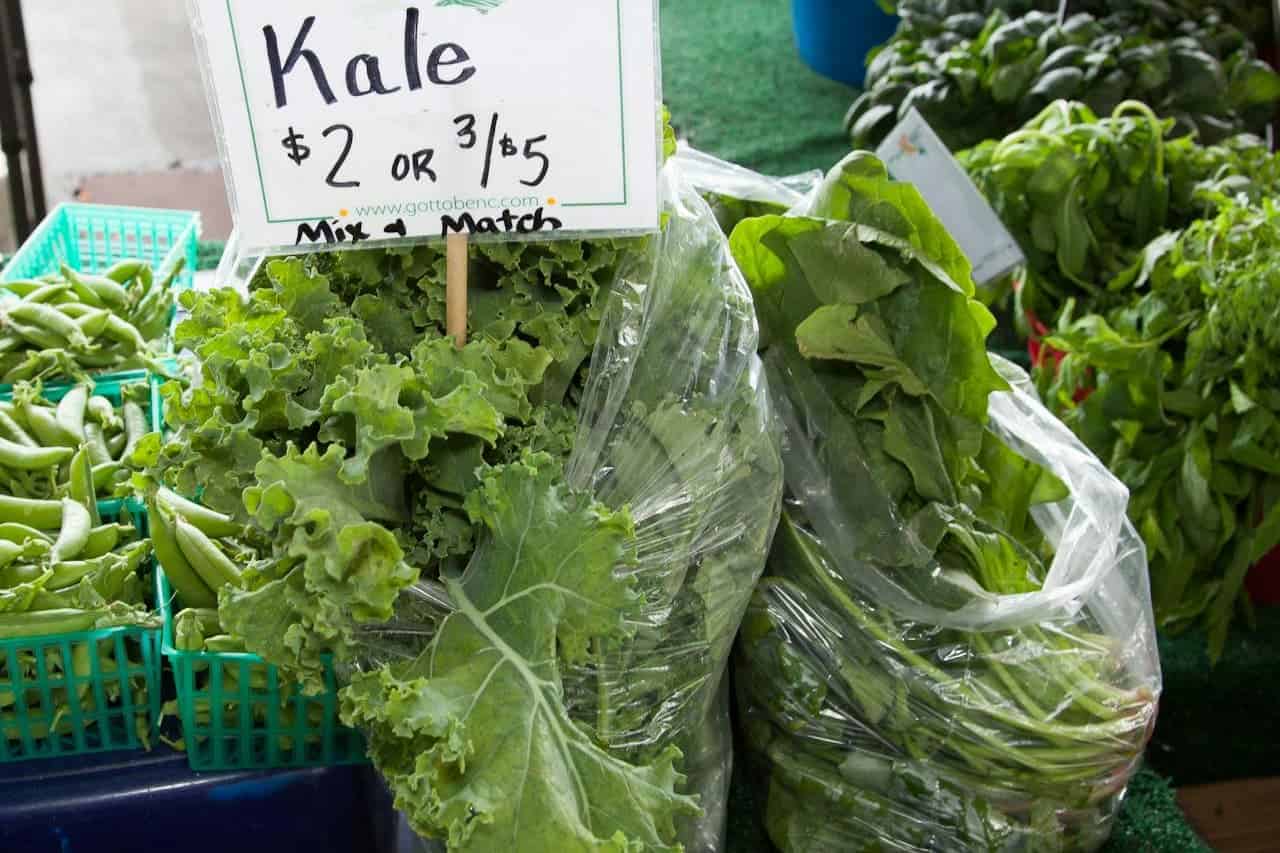 Fresh kale bunches for sale at farmers' market, priced at $2 each or 3 for $5, with "Mix & Match" option and dwarf French beans
