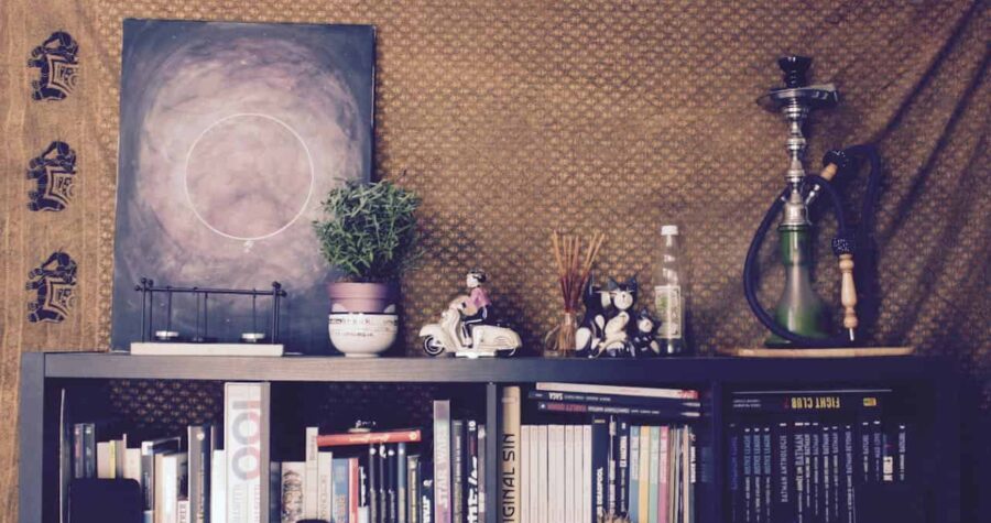 A cozy shelf with books, figurines, a plant, incense sticks, a hookah, and a painting, the background features a patterned cloth, a decorative scene with pop culture references, vibrant and personal display with pop culture items like Star Wars and Marvel comics, creating a casual and creative atmosphere