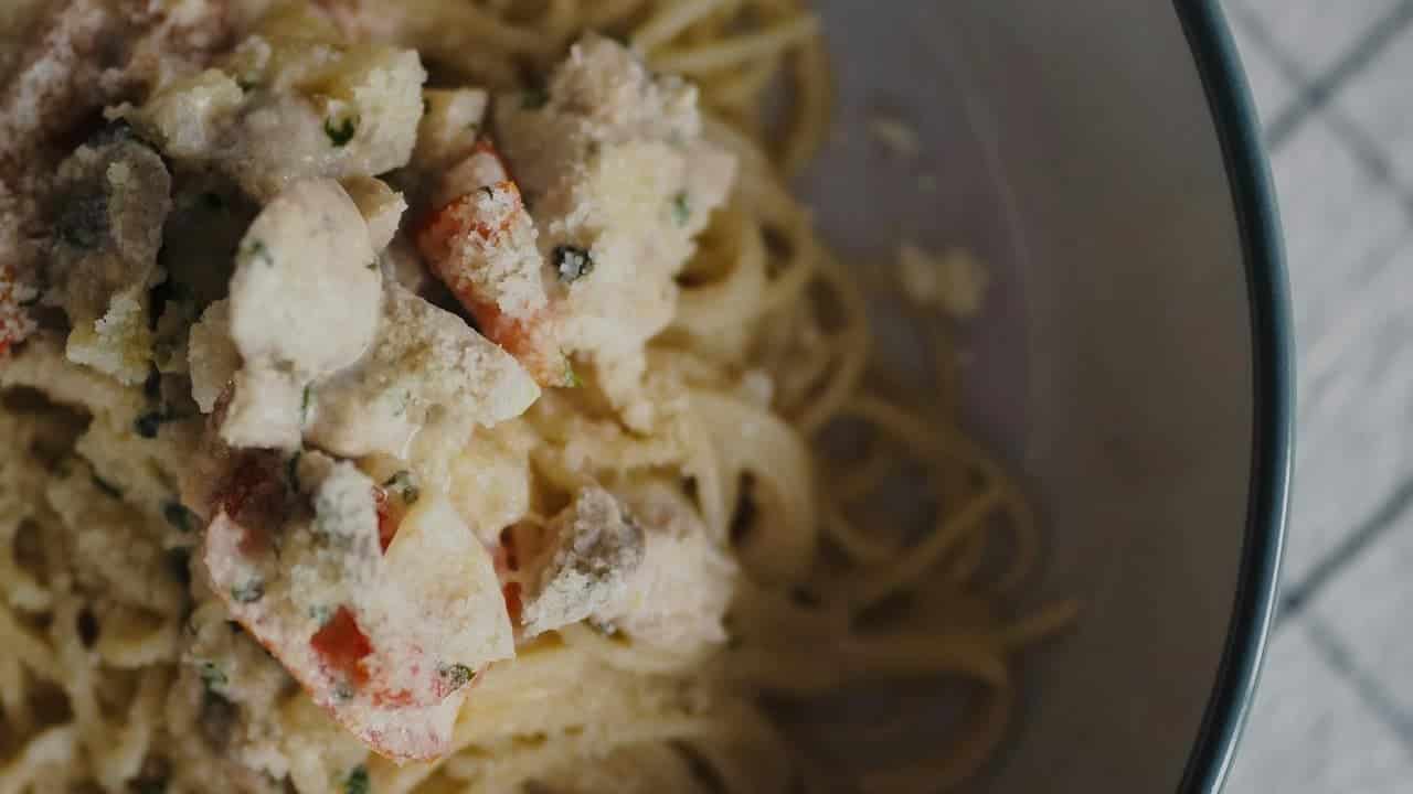 Turkey tetrazzini casserole, pasta mixed with turkey pieces, green peas, topped with melted cheese, golden and bubbly cheese crust, rich creamy sauce, baked in a clear glass dish, comforting meal, savory dish, close-up view of baked casserole
