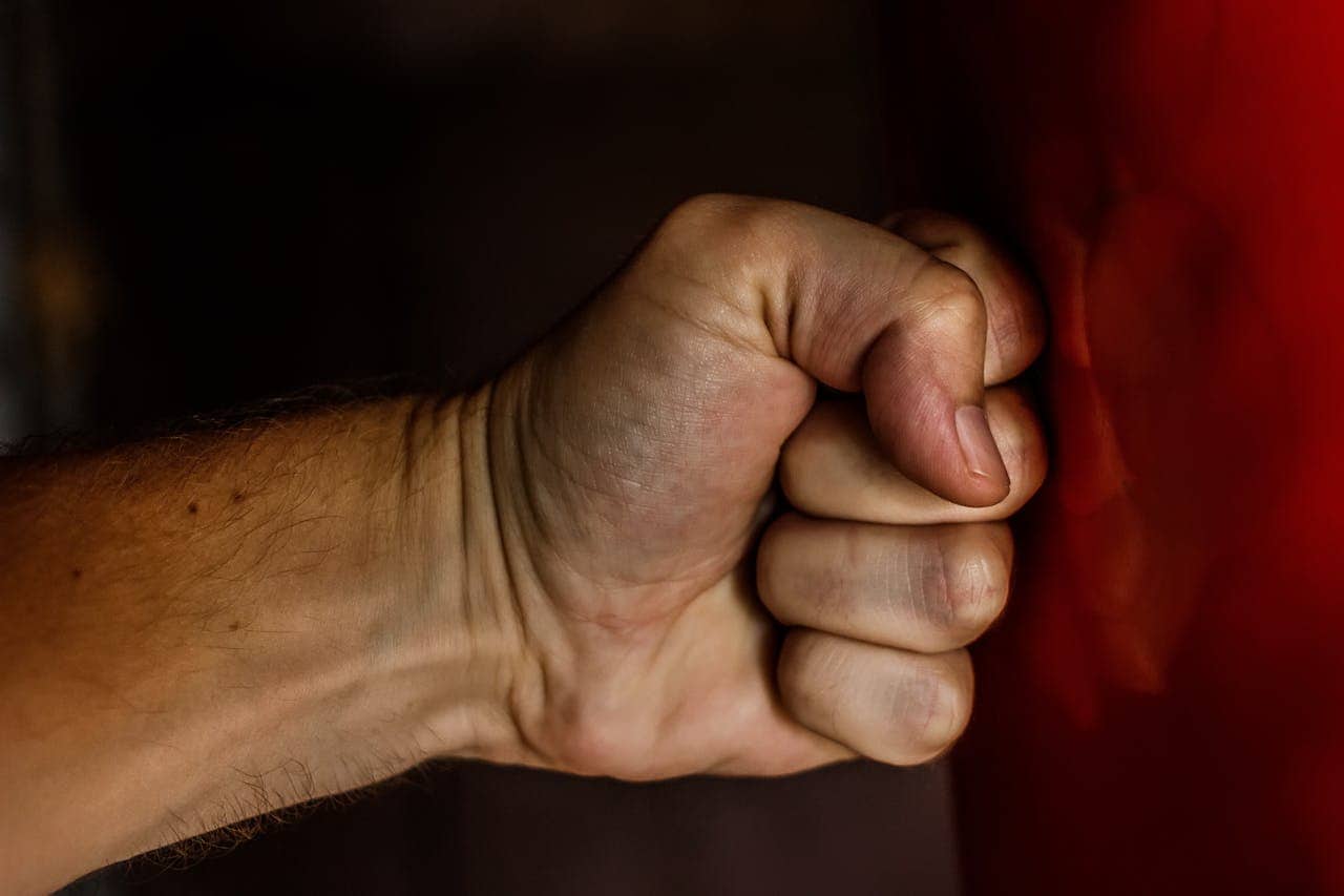 A clenched fist striking a red surface, showing physical exertion or frustration, emphasizing tension or forceful action, possibly in a moment of anger or stress