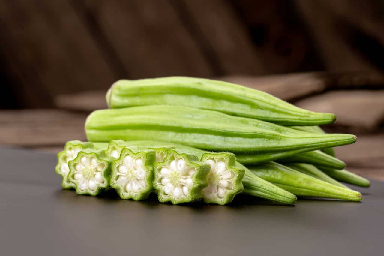 Fresh okra pods arranged on dark surface with several cross-sectioned pieces showing white seeds and star-shaped interior pattern