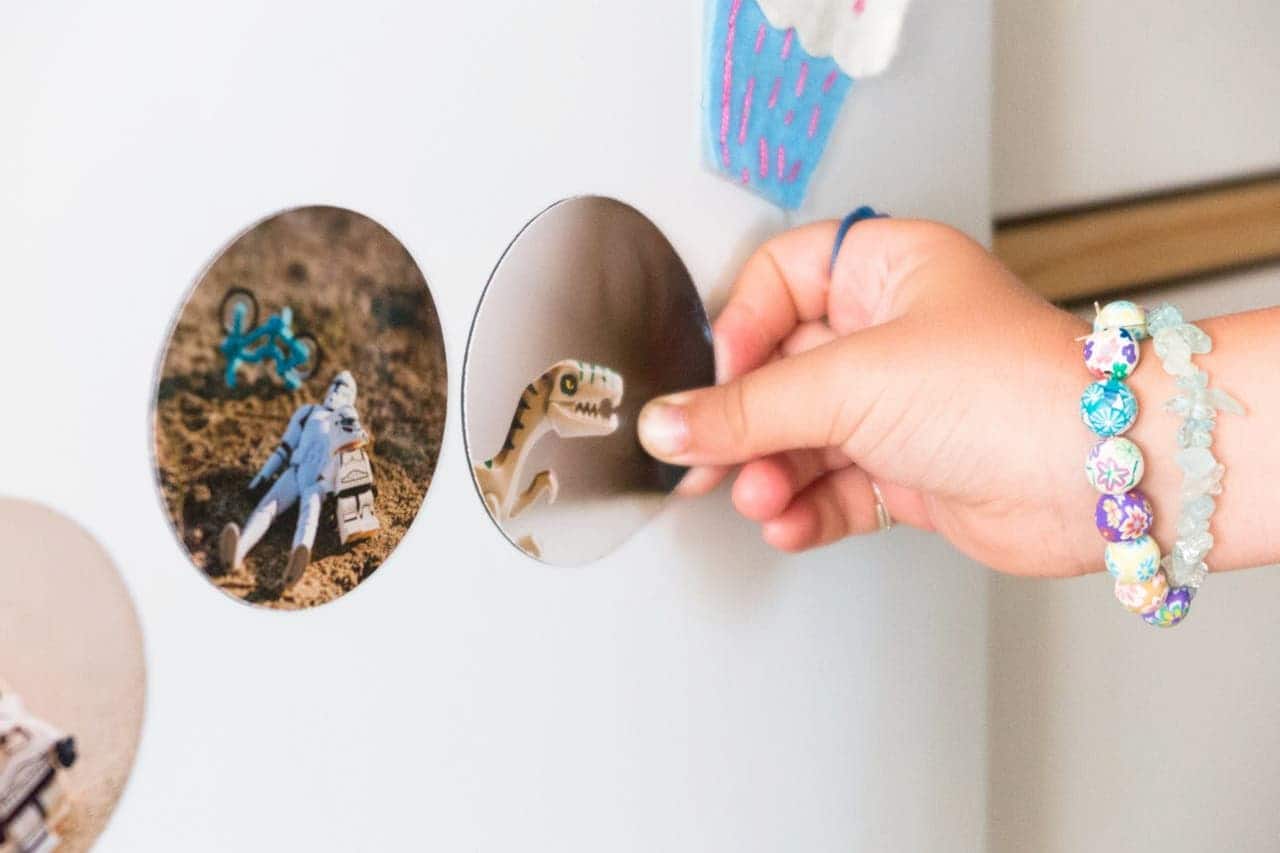 Child's hand wearing colorful bracelets touching a round magnetic display containing a toy dinosaur and LEGO figurine