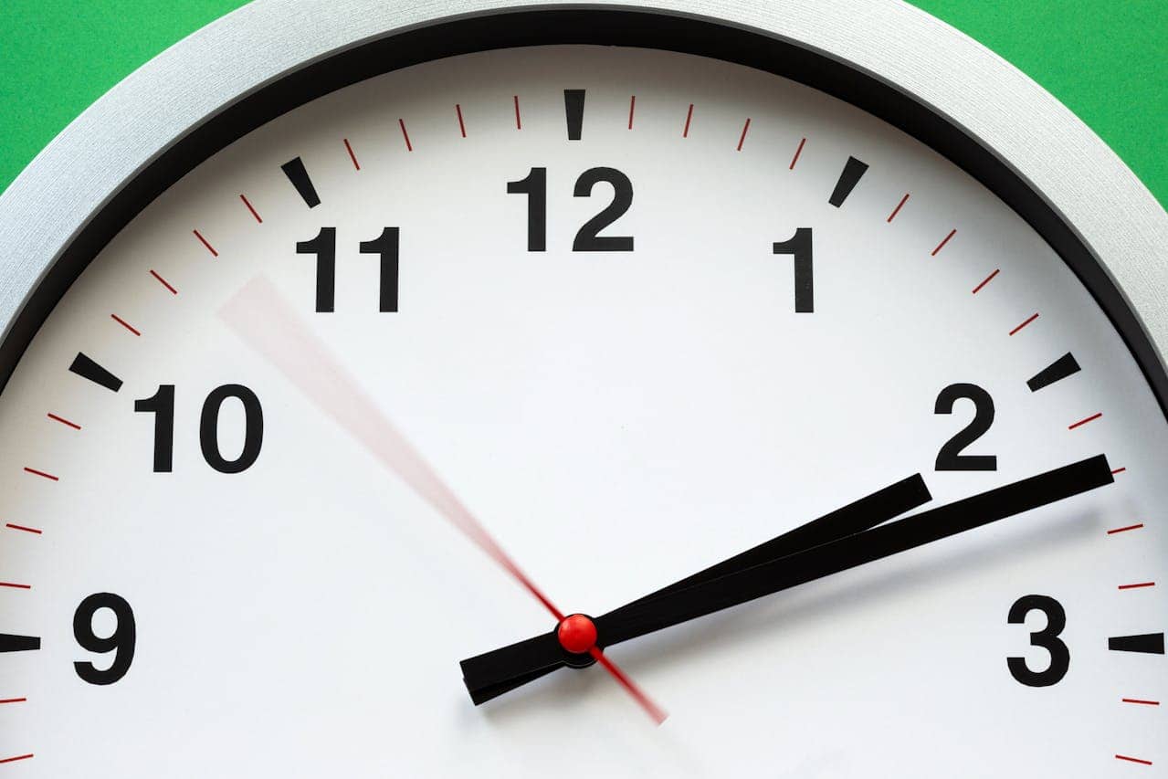 A close-up view of a white wall clock with black and red markings, showing the time just before 2 o'clock, the second hand in motion, with a green background and a red center dot on the clock's hands, capturing the dynamic motion of the clock