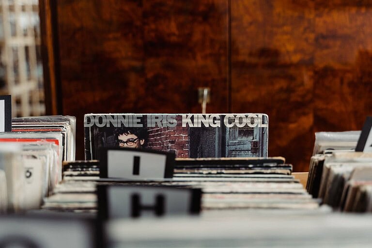 The image shows a vinyl record collection with the album "King Cool" by Donnie Iris in the center, the album is partially visible with the title clear, the records are arranged alphabetically, the image is taken from a low angle focusing on the records in the foreground