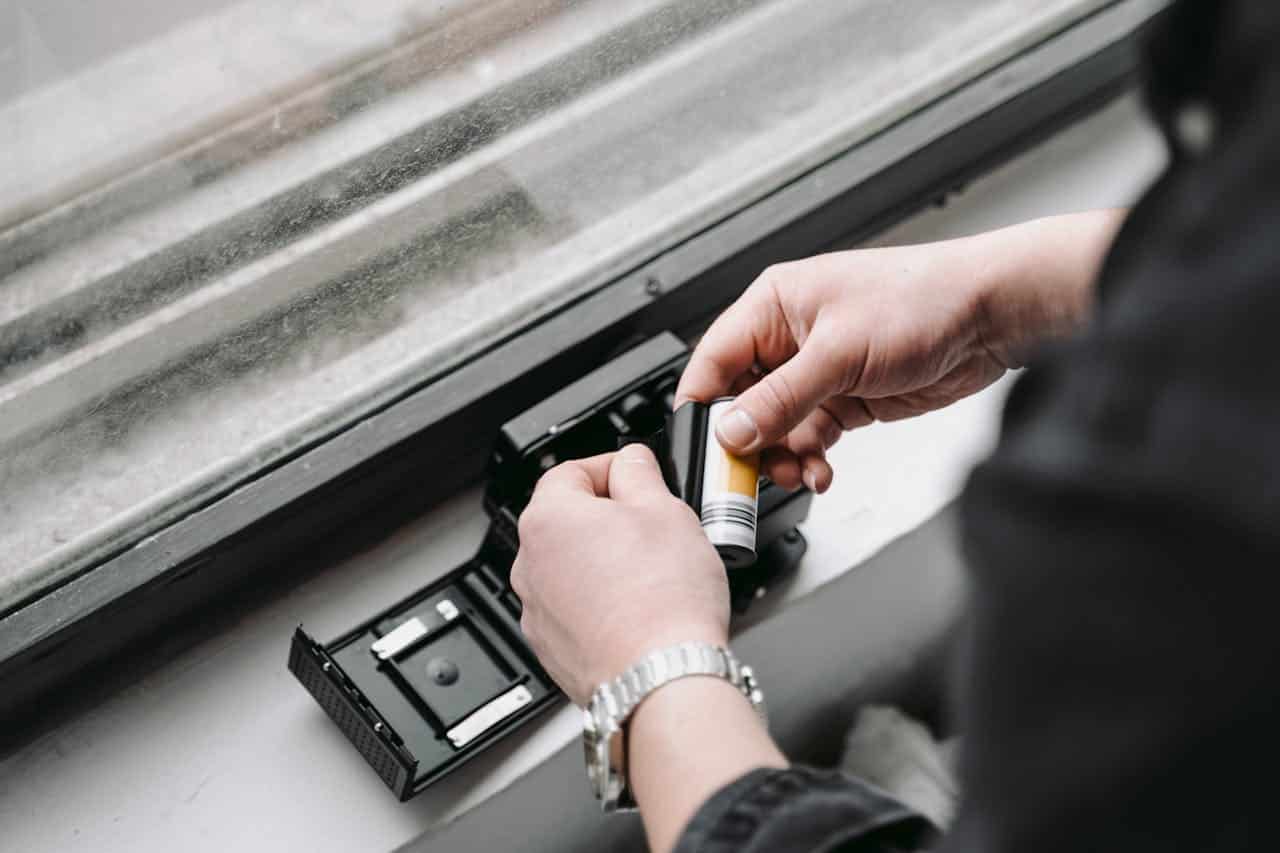 Person loading a roll of film into an open black camera by a window with natural light coming through