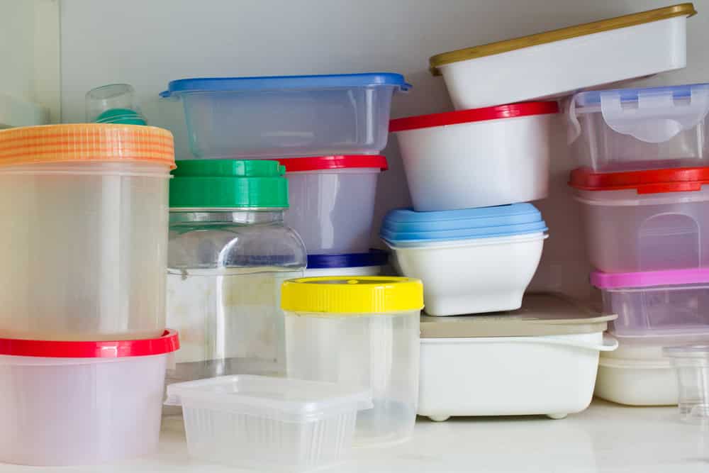 Collection of plastic food storage containers with colorful lids stacked and organized on white kitchen cabinet shelf