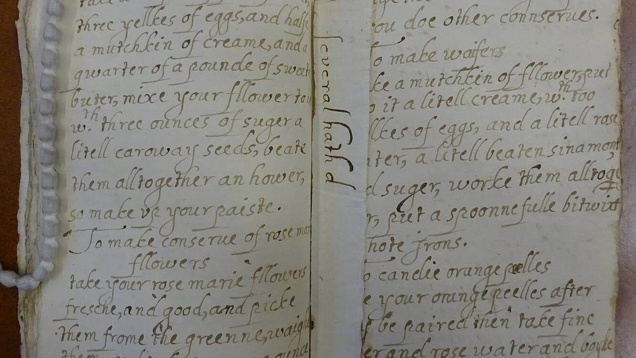 Open antique recipe book showing handwritten cooking instructions for flower conserves and wafers in faded brown ink on aged paper
