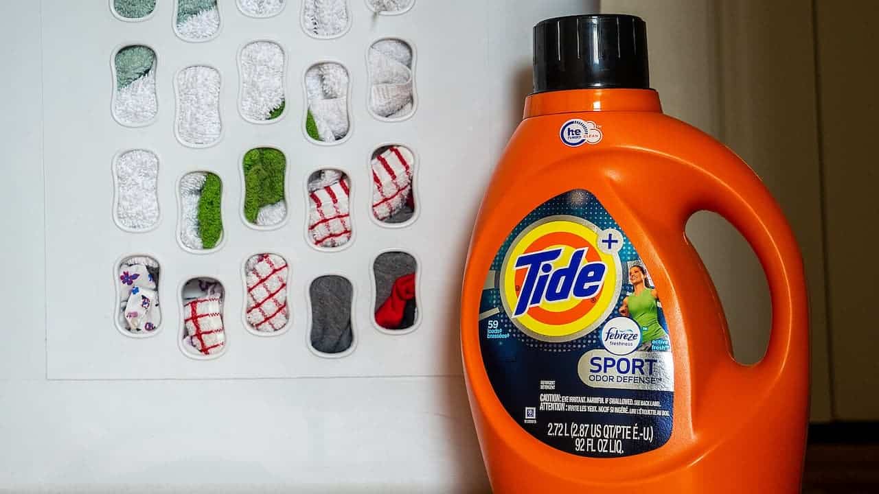Orange Tide Sport laundry detergent bottle next to display card showing various fabric swatches in different colors and patterns