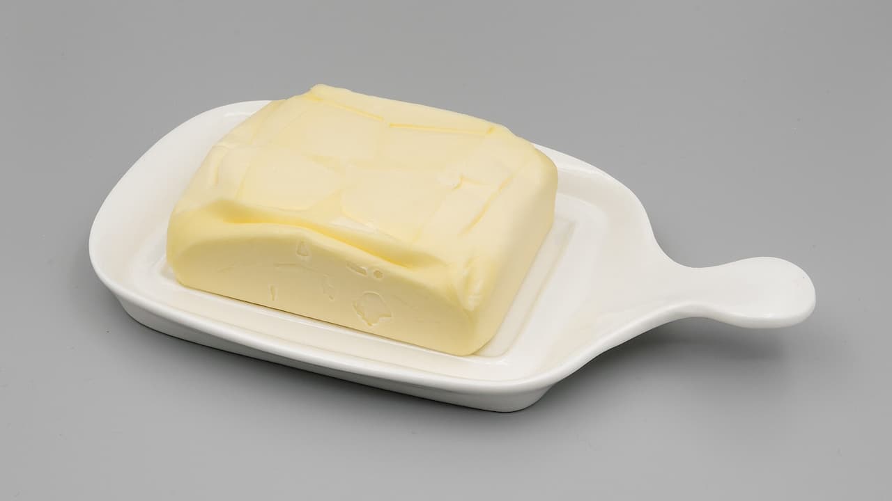 Rectangle of pale yellow butter on white ceramic dish with handle, displayed against neutral gray background