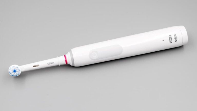 White Oral-B electric toothbrush with blue bristled brush head and pink accent ring on neutral gray background