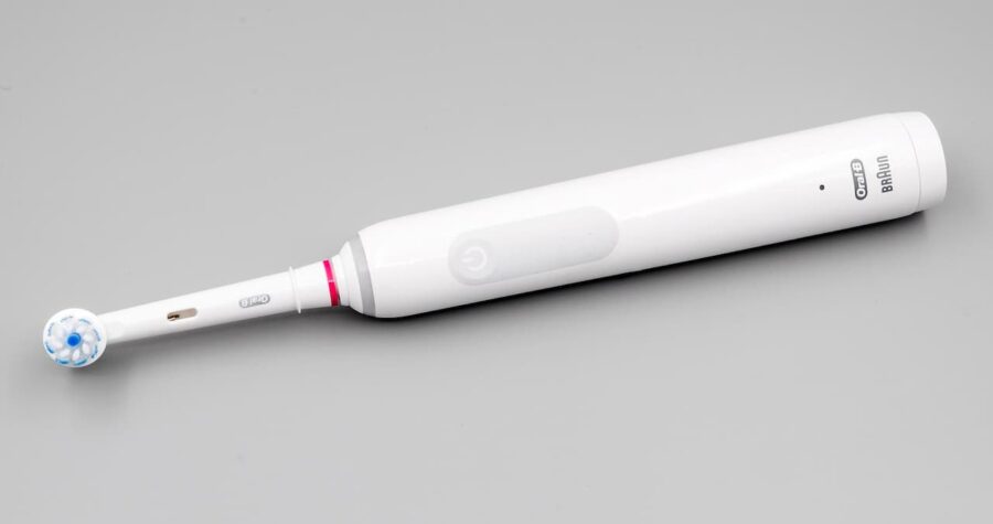 White Oral-B electric toothbrush with blue bristled brush head and pink accent ring on neutral gray background