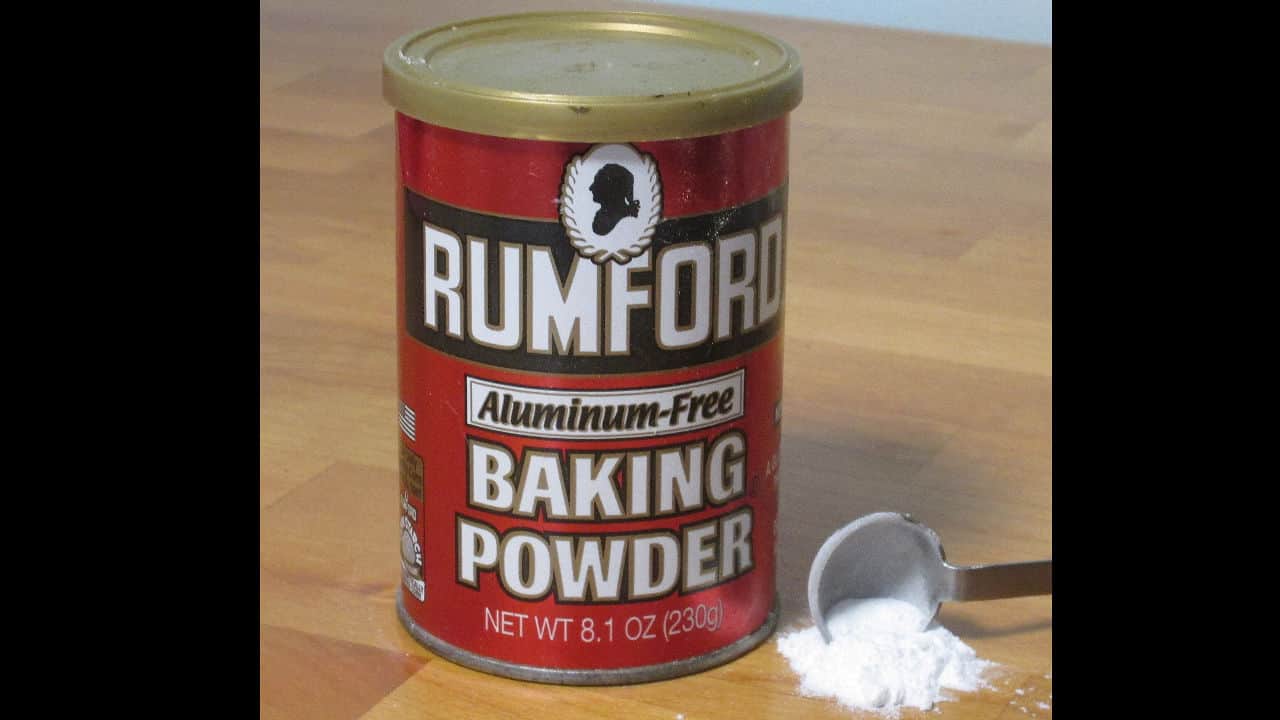 A red can of Rumford aluminum-free baking powder placed on a wooden surface with a measuring spoon of powder beside it