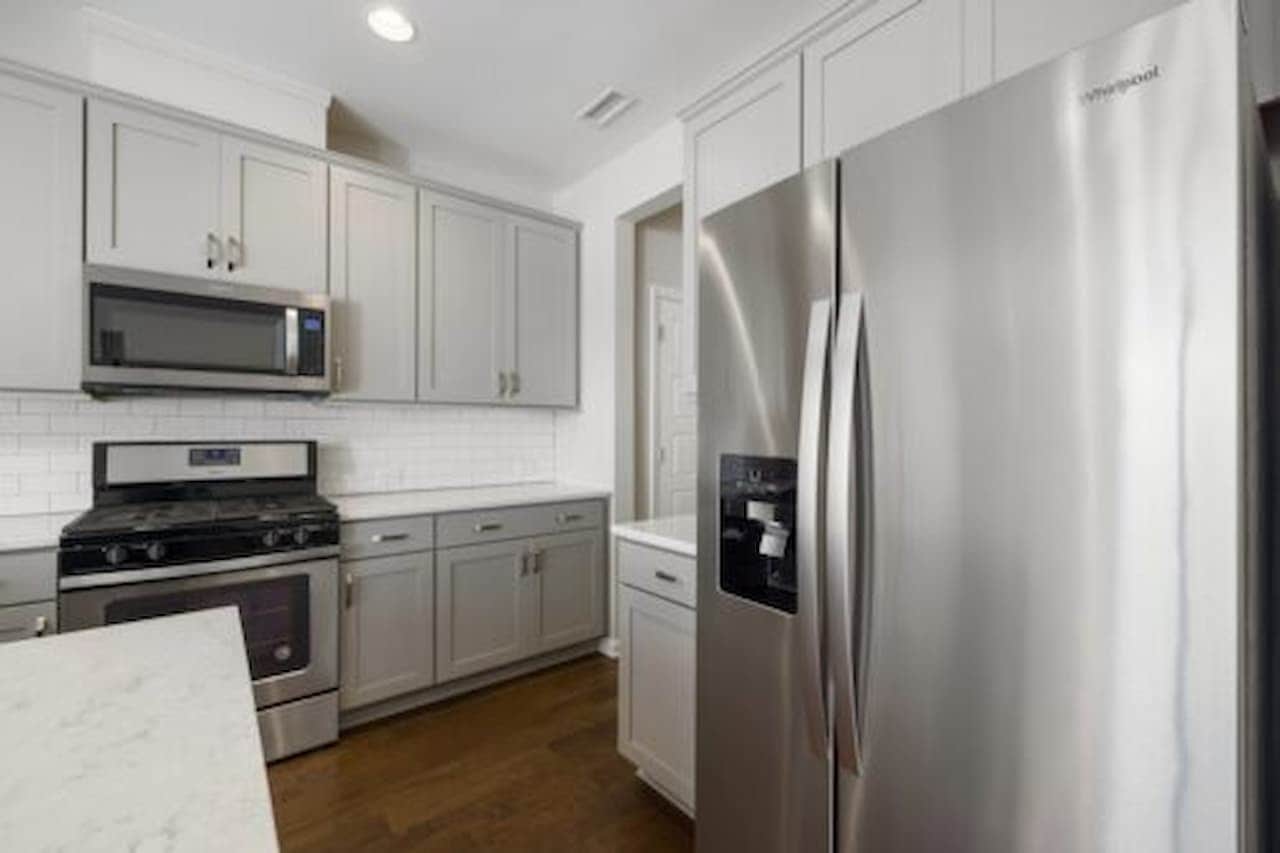 Modern kitchen with built-in stainless-steel appliances, built-in microwave above a gas stove, white subway tile backsplash, marble countertop, recessed ceiling lighting, contemporary and functional design