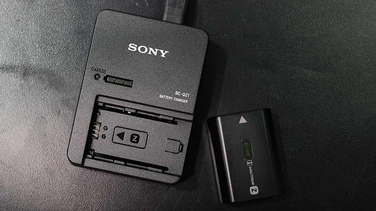 Sony camera battery charger with a compatible battery placed beside it on a dark surface, connected via USB cable