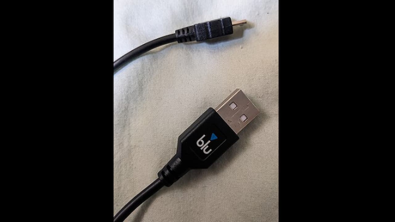 A black Blu USB cable with a USB-A connector and a micro-USB connector, placed on a light-colored fabric surface