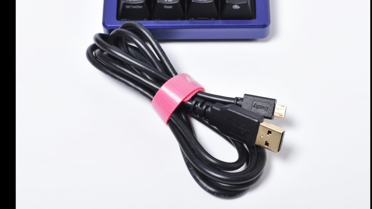 A black Blu USB cable with a USB-A connector and a micro-USB connector, placed on a light-colored fabric surface