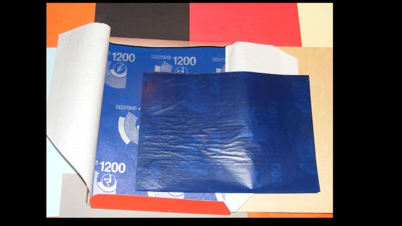 A box containing sheets of blue carbon paper with "1200" and branding printed on them, partially opened to show the shiny coated side used for transferring text
