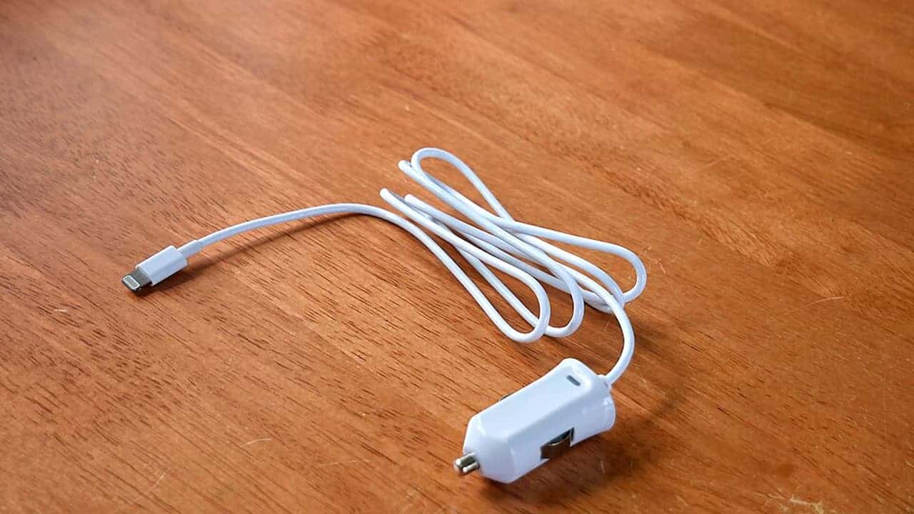 White car charger cord with a Lightning connector on one end and a 12V plug on the other, coiled and placed on a wooden surface