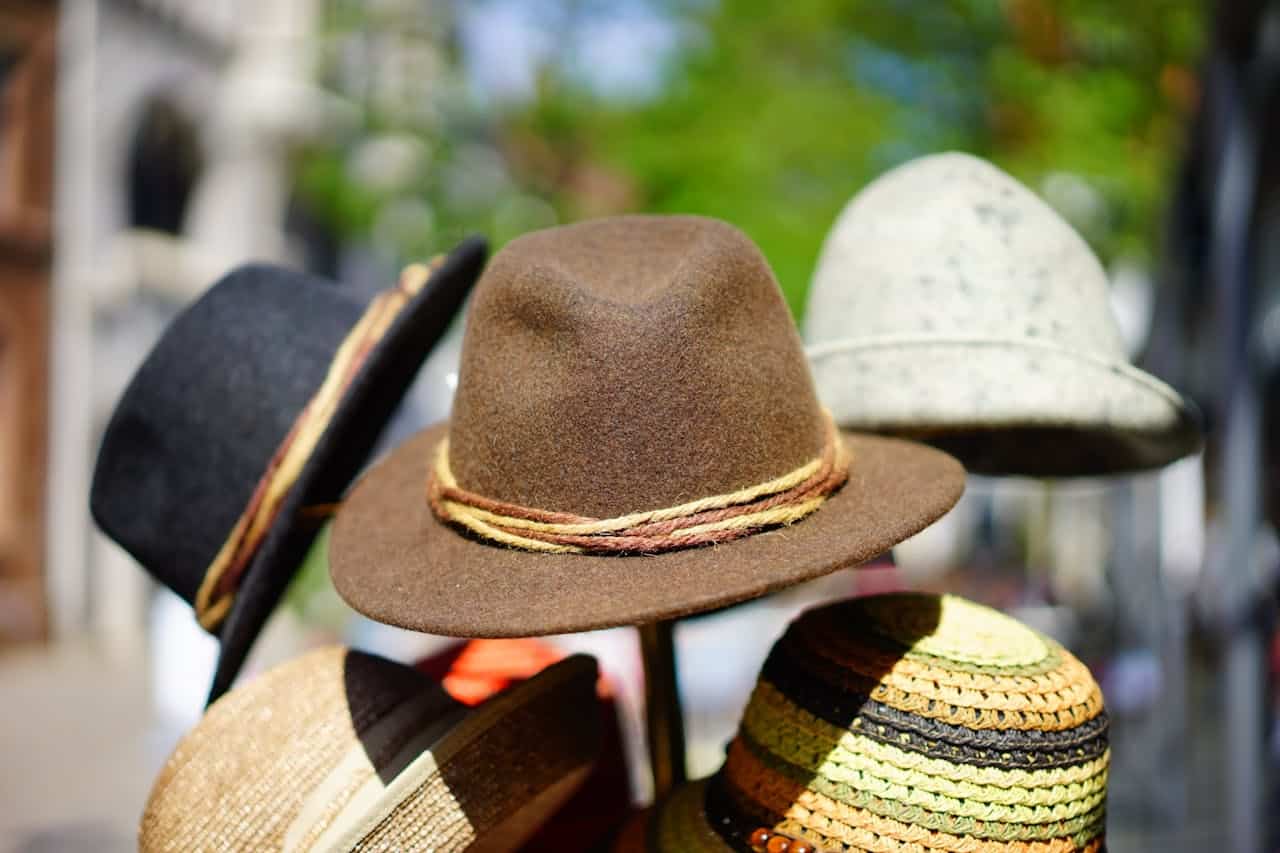Variety of colorful hats displayed outdoors on a stand, including felt, woven, and straw styles in natural lighting